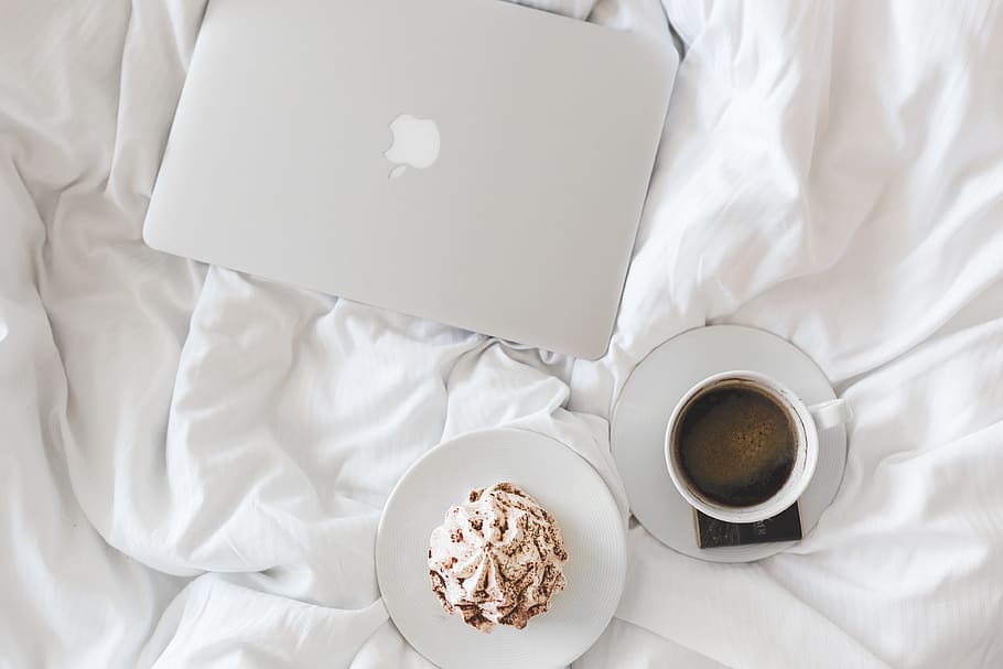 Picture of a bed with a coffee, a cupcake and a computer over it
